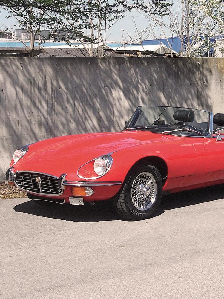 Ein roter Jaguar E-Type steht in der Sonne vor einer Mauer