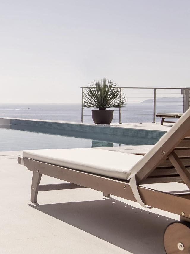 Ein Holzliegestuhl am Pool mit herlichem Ausblick auf das Meer.