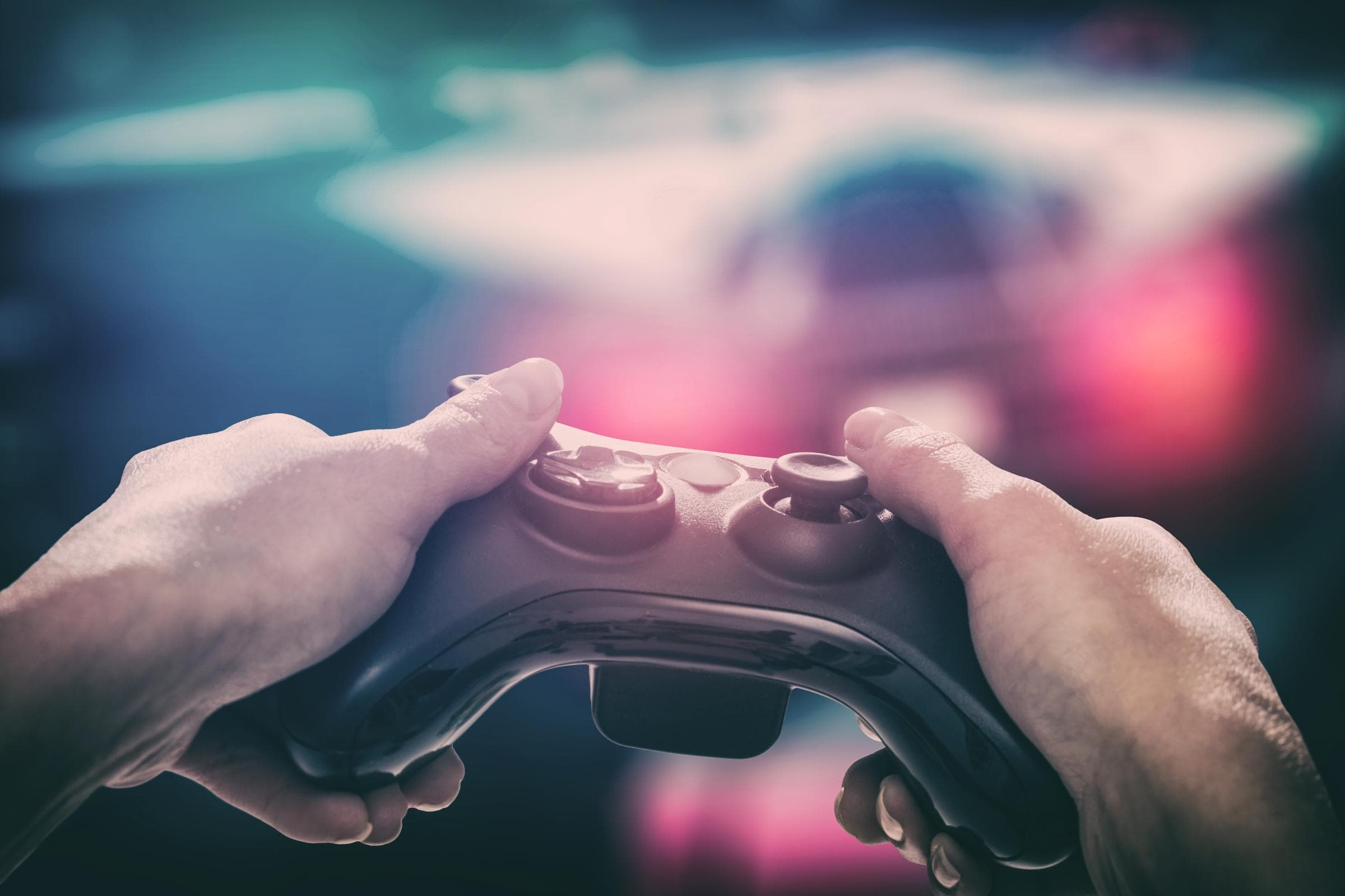 Eine Person hält einen Videospiel-Controller mit beiden Händen, während im Hintergrund ein Rennspiel auf einem Bildschirm zu sehen ist.