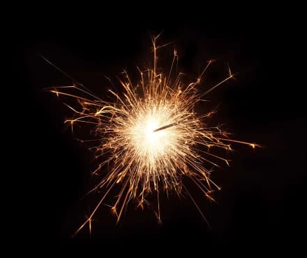 Leuchtende Wunderkerze mit goldenen Funken vor dunklem Hintergrund.