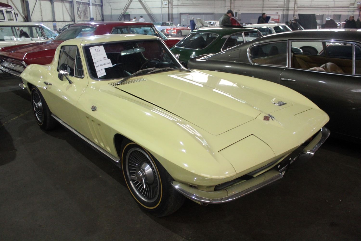 Ein beiger Chevrolet Corvette 1966 parket in einer Lagerhalle neben weiteren Oldtimern. 