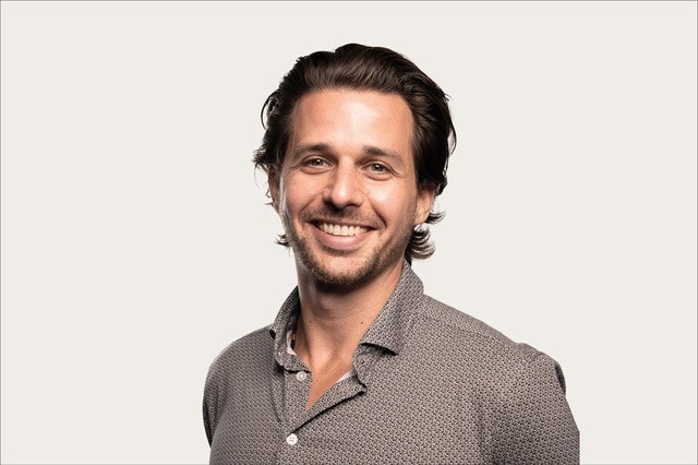 Eric Insel, KI-Dozent und KI-Sparringspartner für Unternehmen, trägt ein blaugemustertes Hemd und lacht in die Kamera 