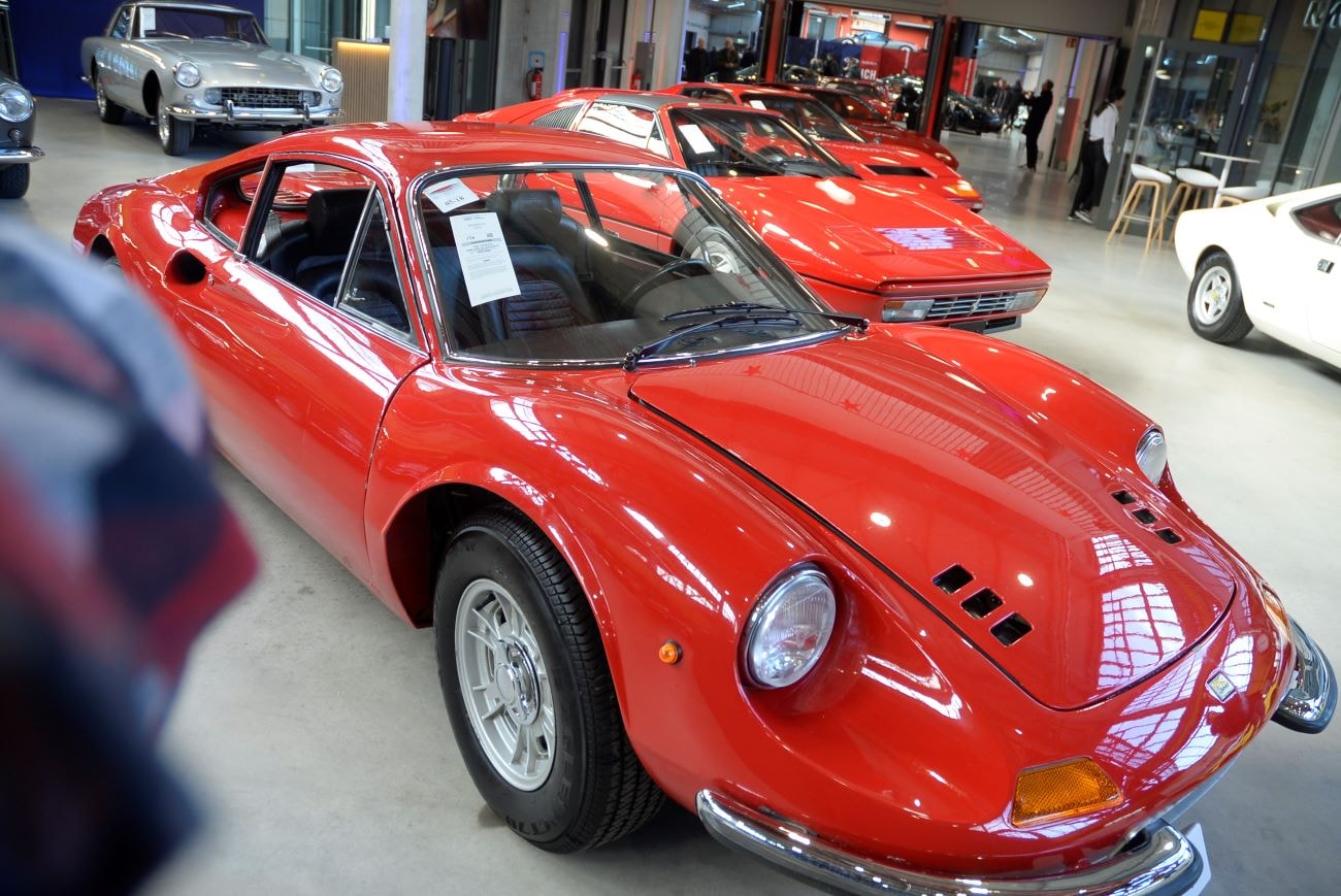 Ein rot glänzender Ferrari Dino von 1973 parket in einer Halle mit weiteren Oldtimern.