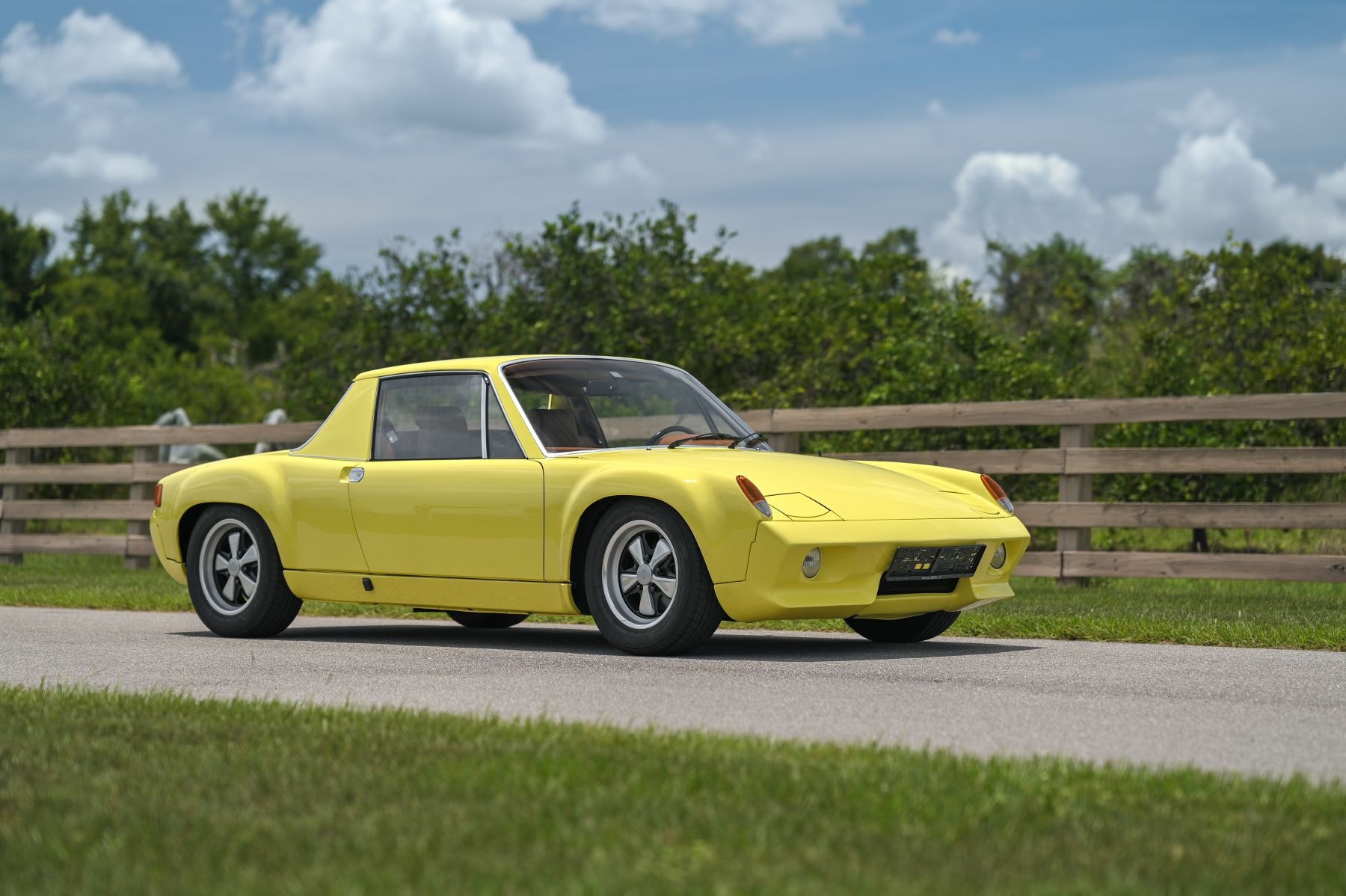 Einer der 9 Exemplare des gelben Porsche 916 fährt auf einer Straße an einem Feld vorbei.