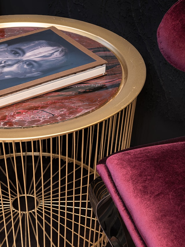 Auf einem goldenen Beistelltisch liegt ein Coffee Table Book, daneben steht ein roter, samtener Loungesessel