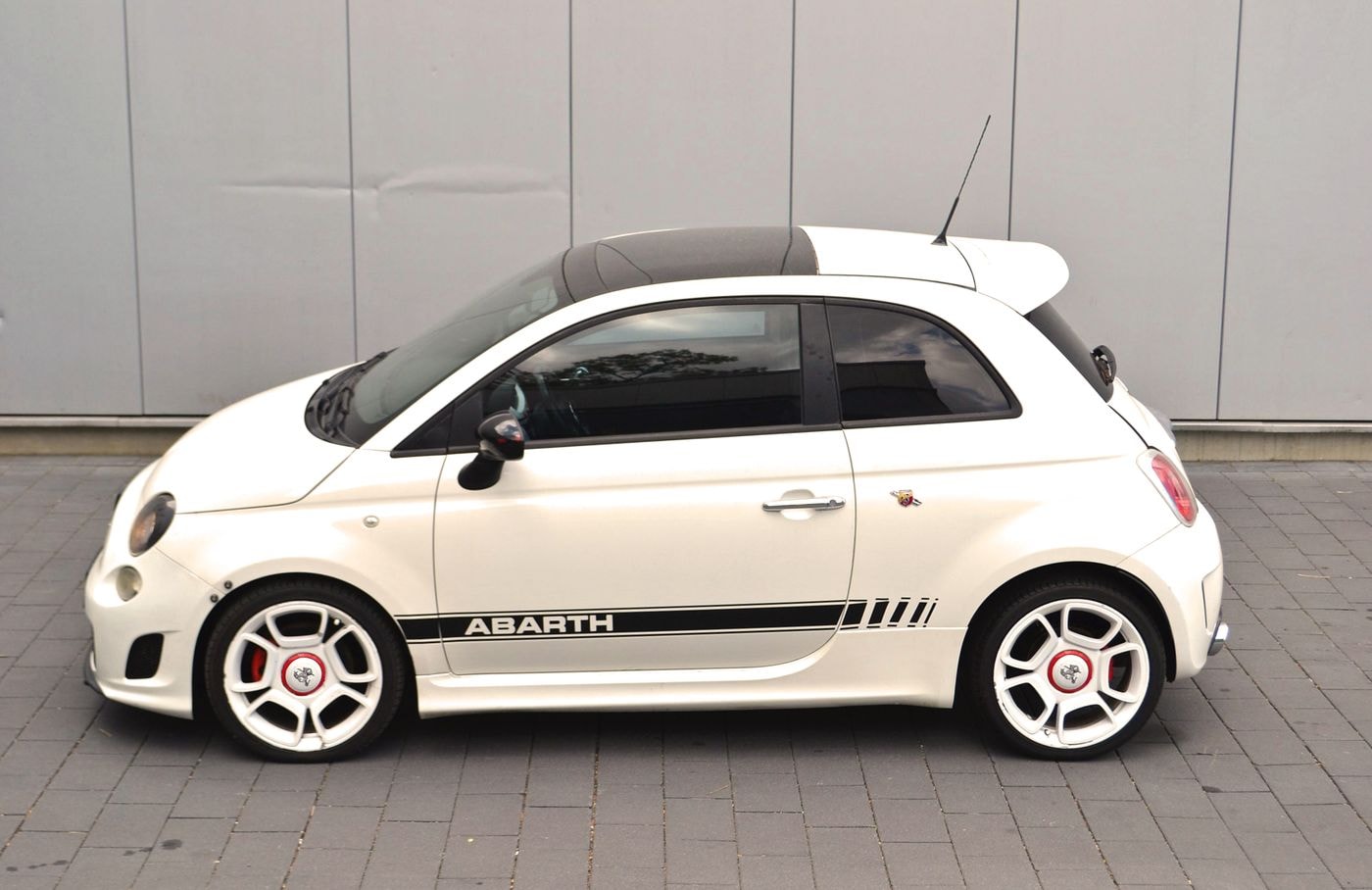 Silhouette eines weißer Fiat Abarth 500 mit schwarzen Details parkend vor einer grauen Wand.