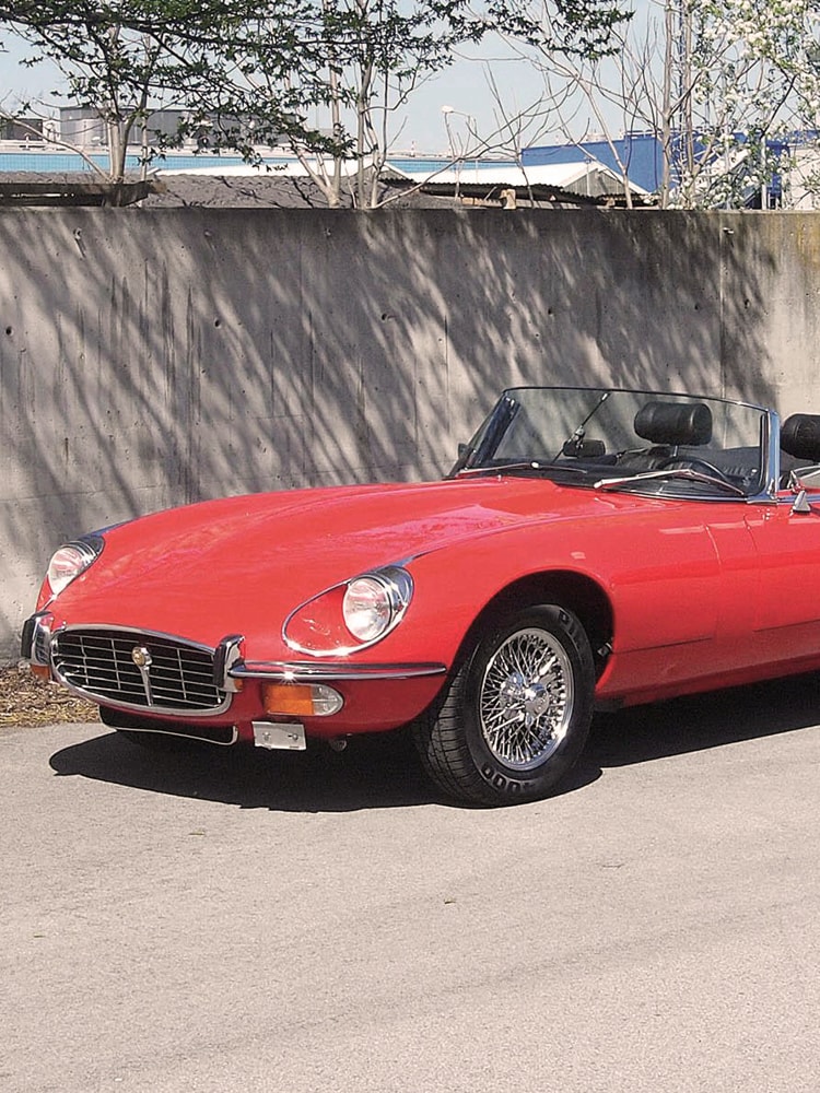 Ein roter Jaguar E-Type steht in der Sonne vor einer Mauer