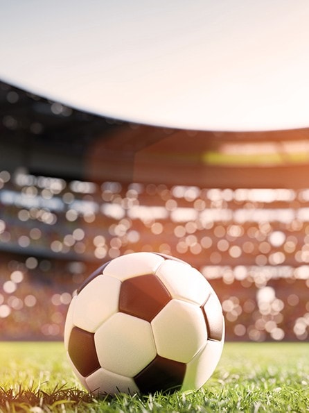 Fußball liegt auf grünem Rasen in einem vollen Fußballstadion mit Zuschauern bei Sonnenschein