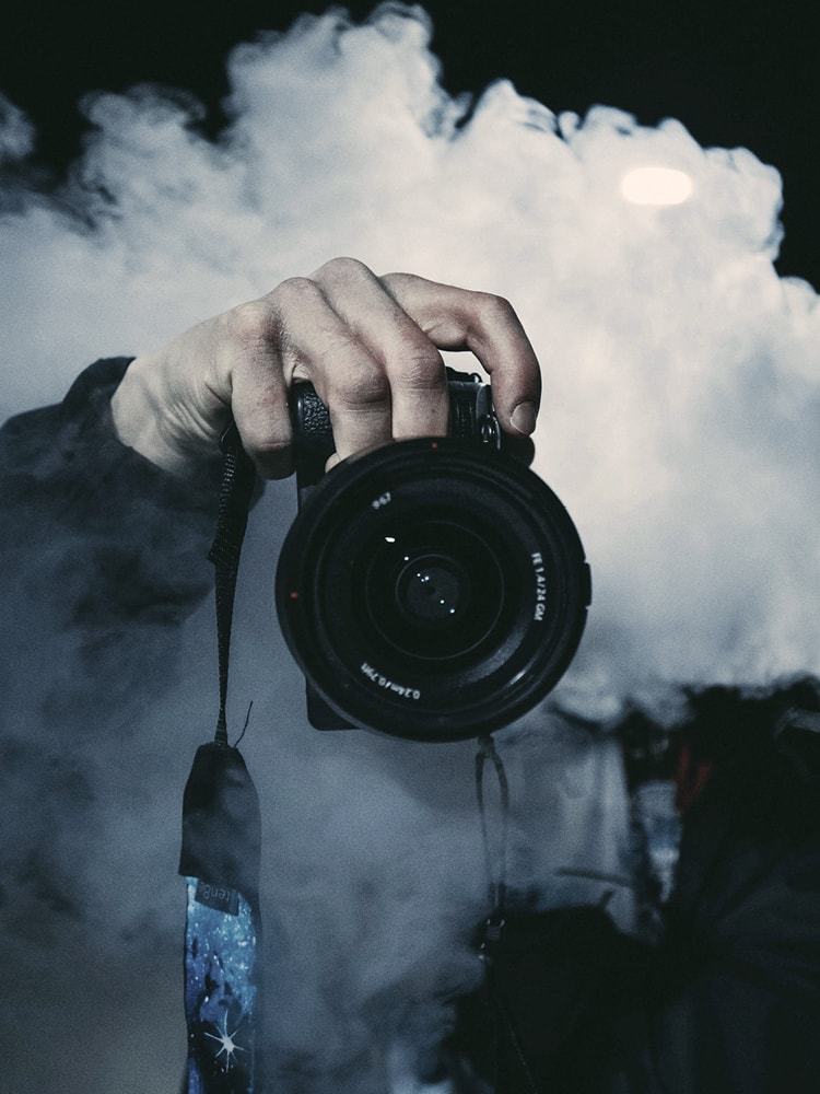 Ein Fotograf macht ein Bild mit seiner Kamera. Man sieht nur seine Hand und den Fotoapparat. Er selbst ist von Nebel verdeckt.