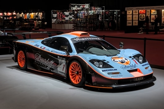 In den Innenräumen ist ein schnittiger Rennwagen McLaren F1 in hellblau-orangefarbenen Tönen ausgestellt. Er besticht durch auffällige Logos und leuchtend orangefarbene Felgen und strahlt eine klassische Rennsportatmosphäre aus.