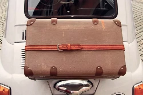 Ein brauner Vintage-Koffer mit Lederriemen ist auf der Rückseite eines klassischen Autos befestigt.