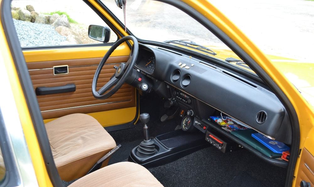 Innenraum eines gelben Oldtimers mit manueller Schaltung, drei Rundinstrumenten, Schaltern und einem alten Radio auf dem Armaturenbrett.