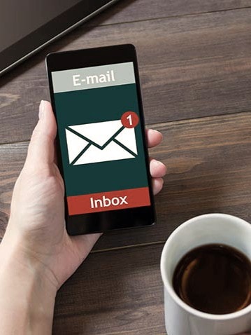 E-Mail-Benachrichtigung auf Smartphone: Person hält Smartphone und Kaffeetasse in der Hand