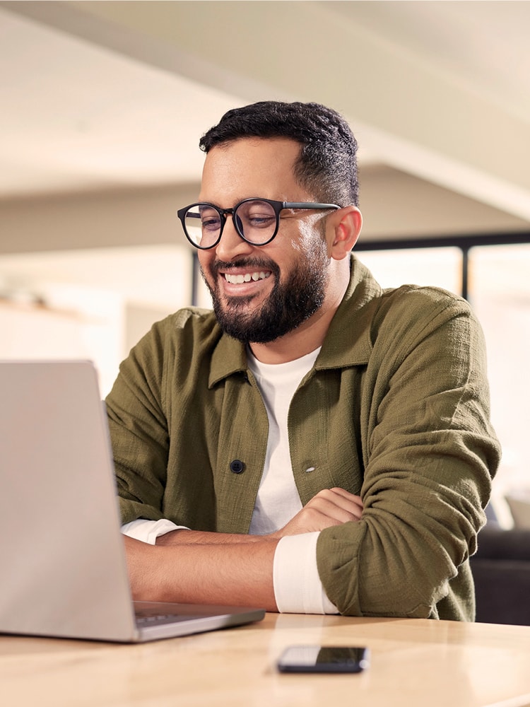 Ein Mann mit Brille und Bart sitzt am Laptop und lächelt