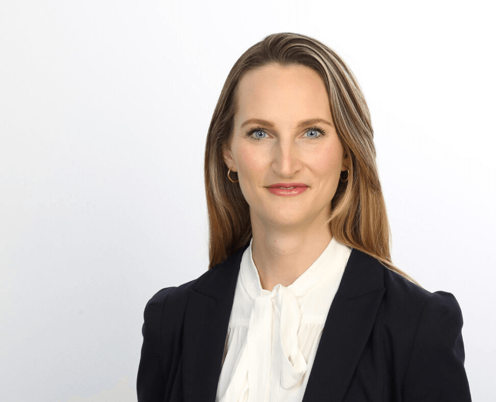 Gisa Kimmerle, eine Frau mit langen Haaren, trägt eine weiße Bluse mit einer Schleife und einen dunklen Blazer. 