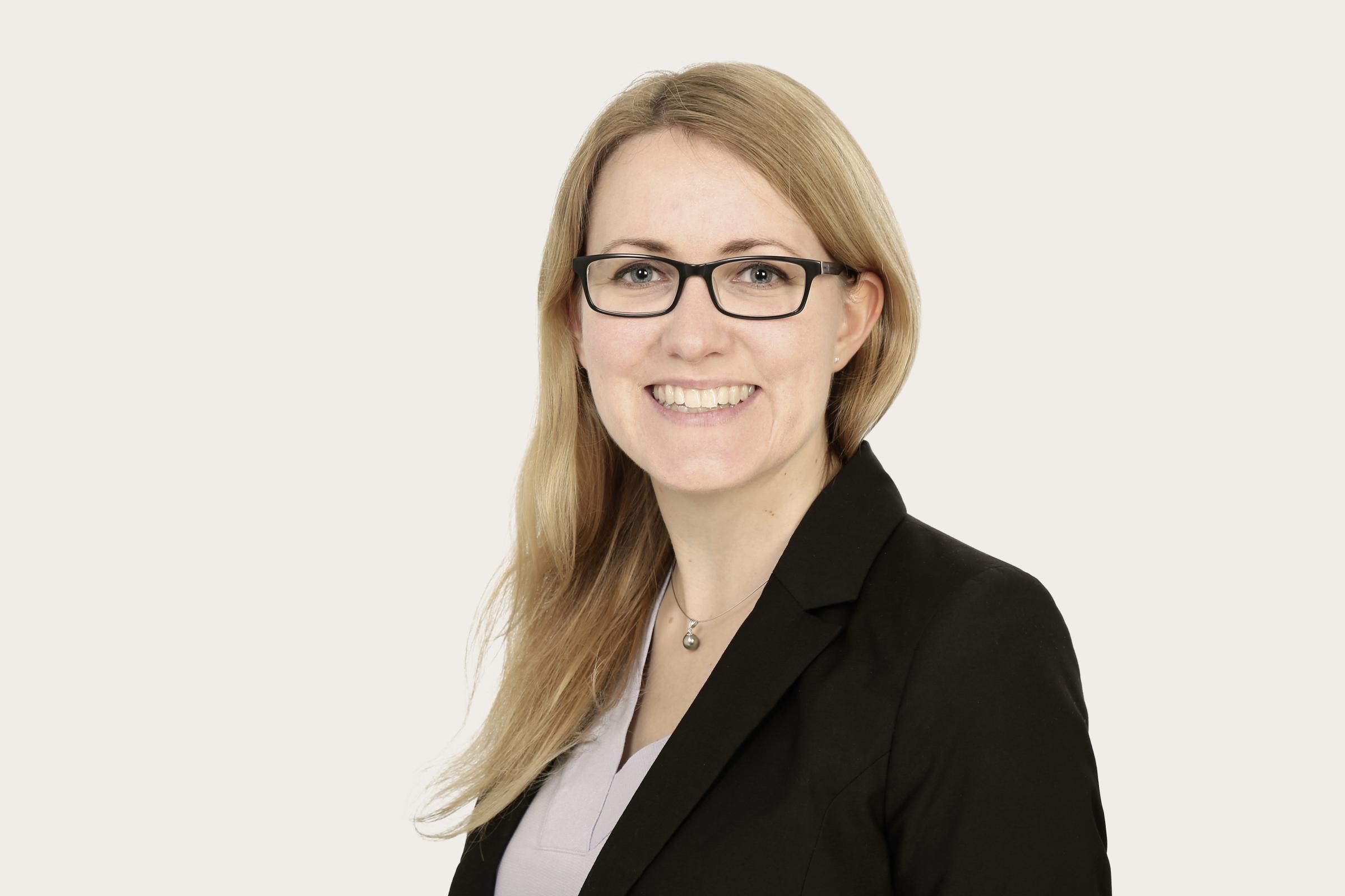 Hannah Täge, eine Frau mit langen blonden Haaren, trägt einen schwarzen Blazer und ein helles Oberteil. 