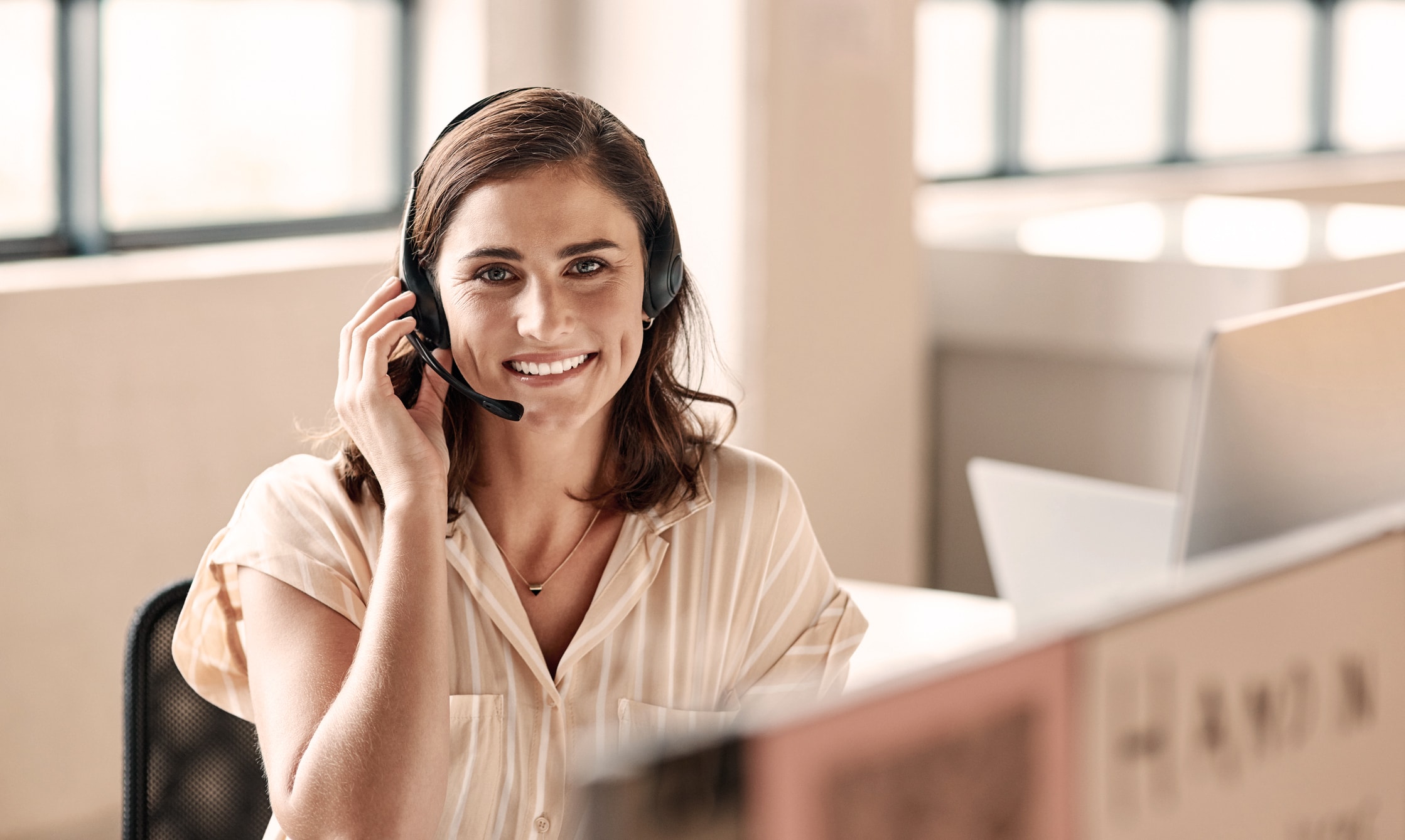 Eine Frau mit Headset sitzt am Computer und blickt in die Kamera