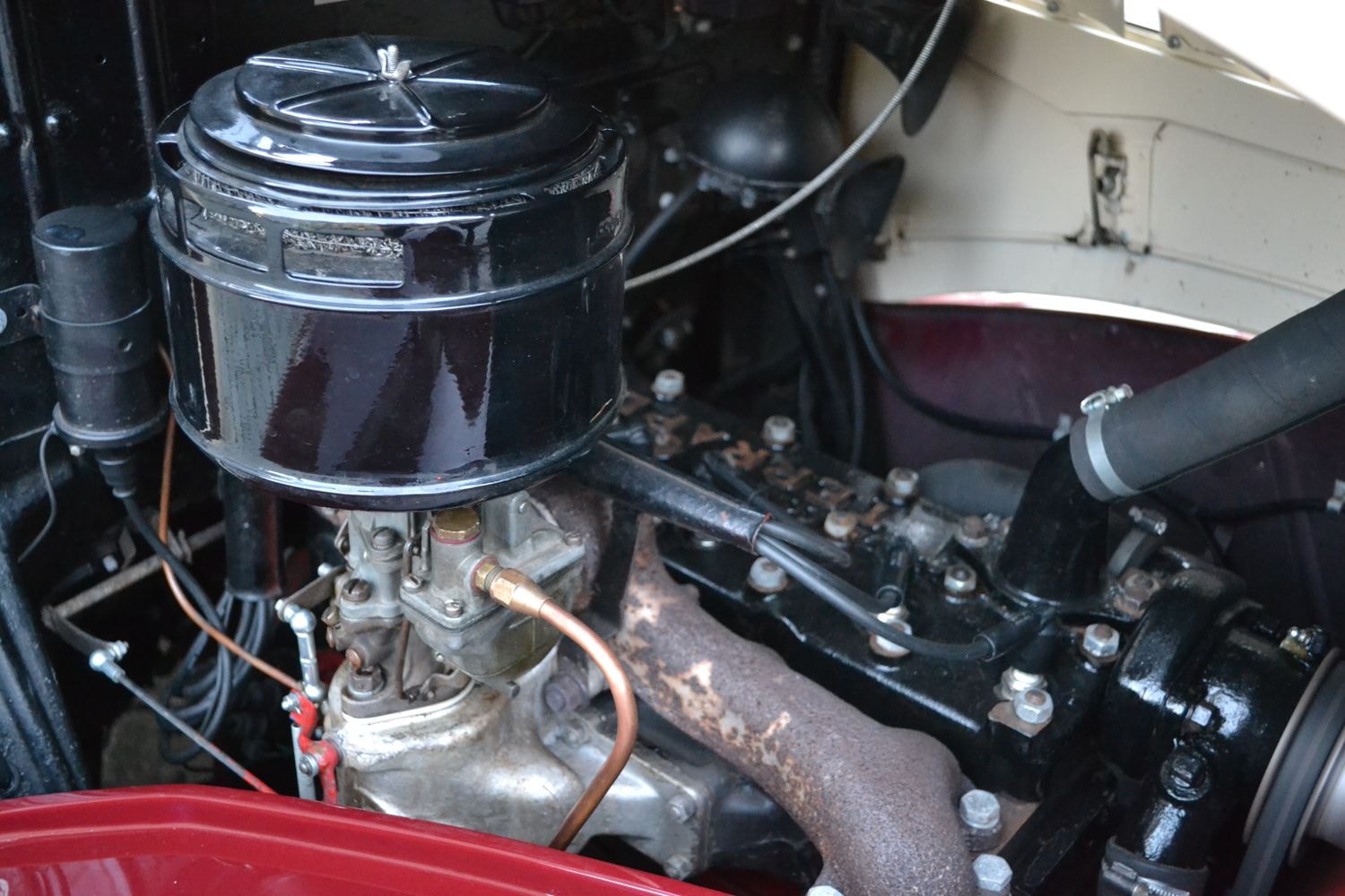 Der Motorraum eines Fahrzeugs, fokussiert auf den Motor. Der Luftfilter ist oben links sichtbar, mit verschiedenen Schläuchen und Metallkomponenten. Der Auspuffkrümmer zeigt Rost und Abnutzung.