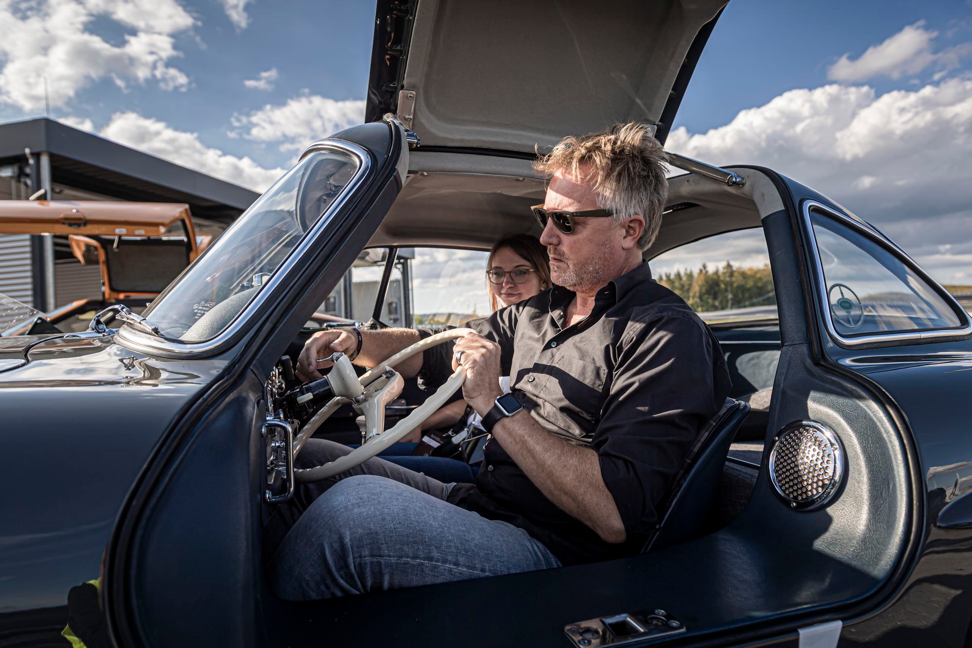 Jenz Tanz sitzt in Mercedes Benz 300 SL mit Beifahrerin und hält weißes Lenkrad fest