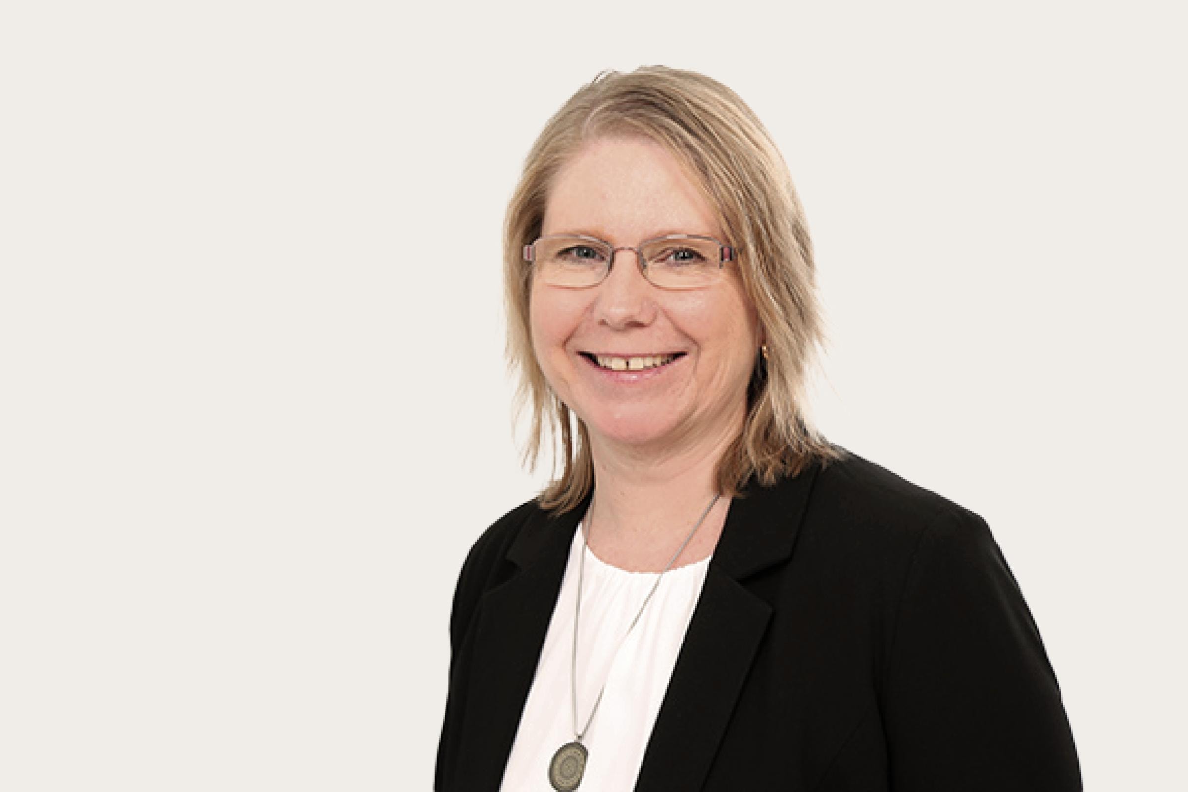 Regina Huber, eine Frau mit schulterlangem Haar, trägt einem schwarzem Blazer und weißem Oberteil.