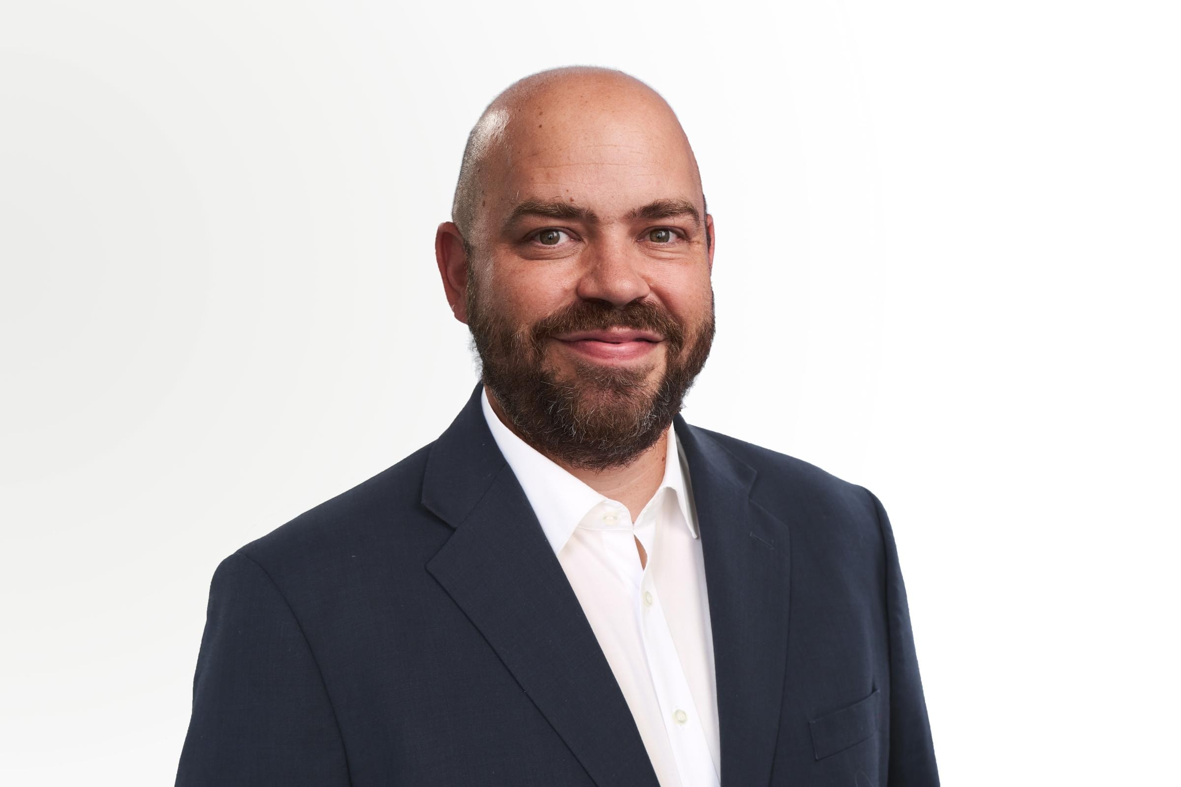 Tobias Wenhart trägt einen dunklen Anzug und weißem Hemd vor weißem Hintergrund.