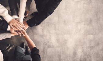 Blick von oben auf eine Gruppe von Menschen, die im Kreis stehen und ihre Hände übereinanderlegen