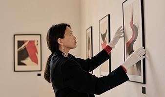 Eine Frau trägt weiße Handschuhe und hängt ein Bild an eine Wand