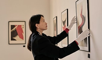 Eine Frau trägt weiße Handschuhe und hängt ein Bild an eine Wand