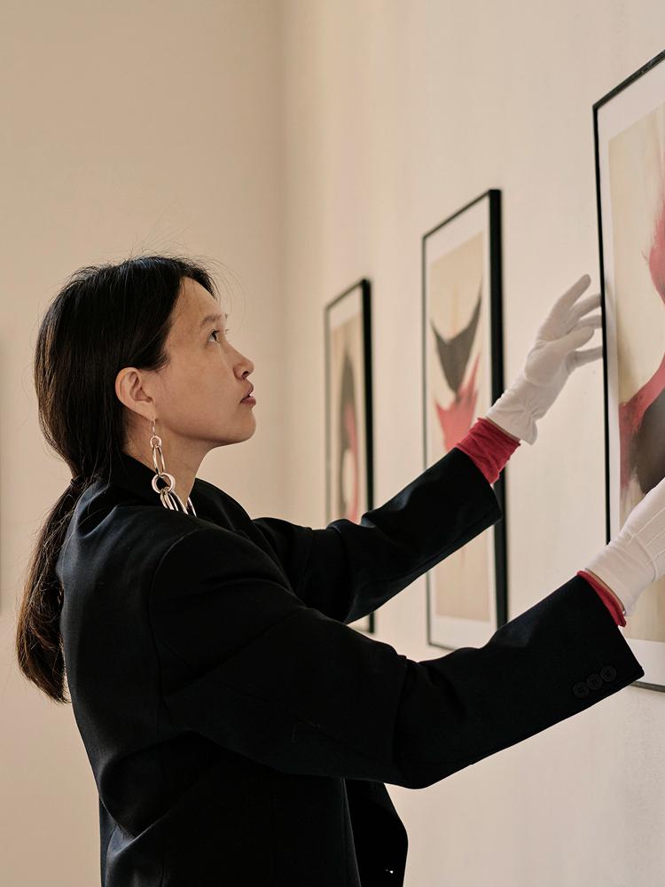 Eine Frau trägt weiße Handschuhe und hängt ein Bild an eine Wand