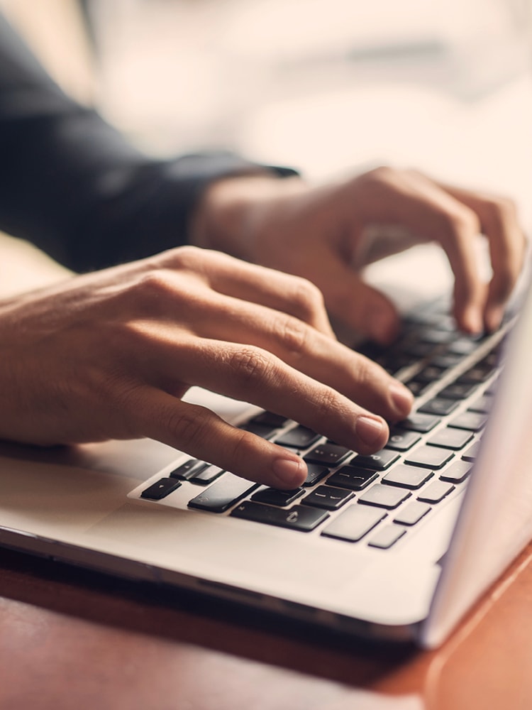 Hände eines Mannes in Anzug, die an einem Laptop arbeiten