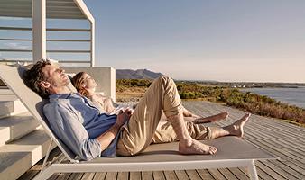 Ein Mann und eine Frau sonnen sich auf Liegen auf einer Terrasse am Meer