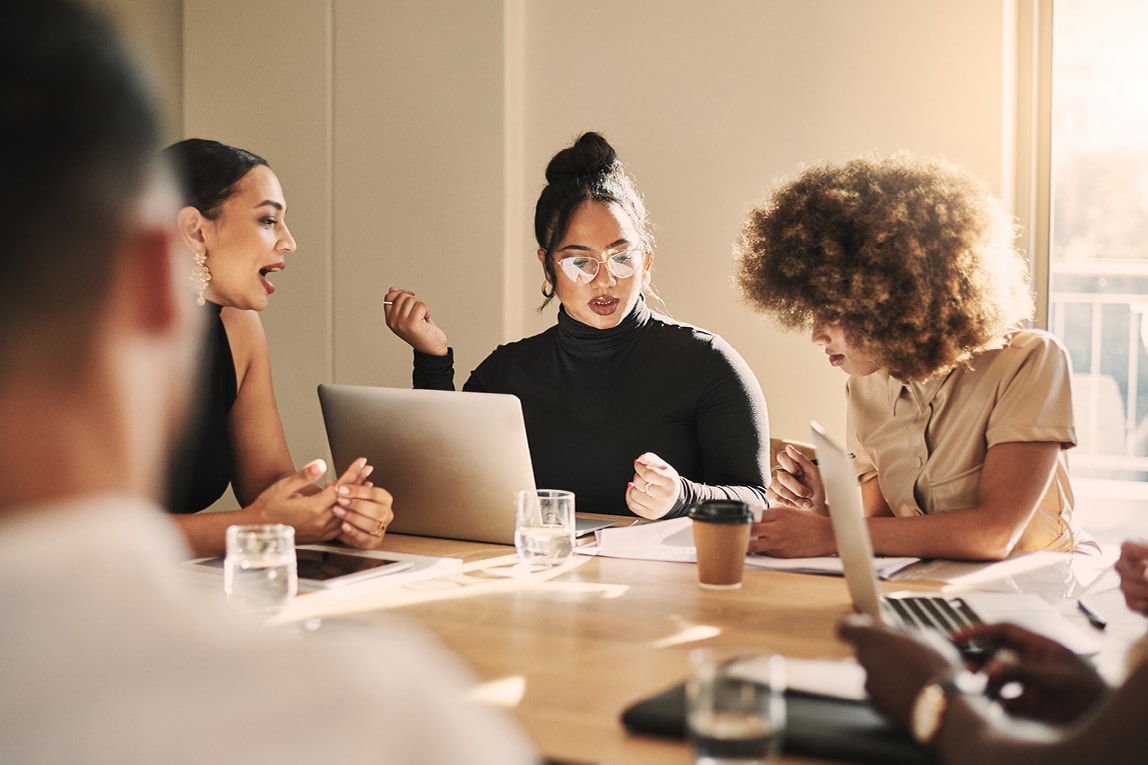 Eine Gruppe von jungen Menschen sitzt an einem Tisch mit Laptops zusammen und arbeiten gemeinsam