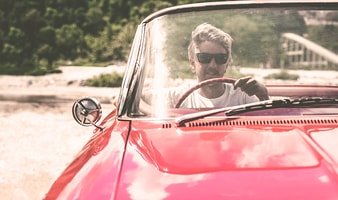 Person fährt ein rotes Cabrio auf einer sonnigen Straße, Blick auf Frontscheibe und Lenkrad.