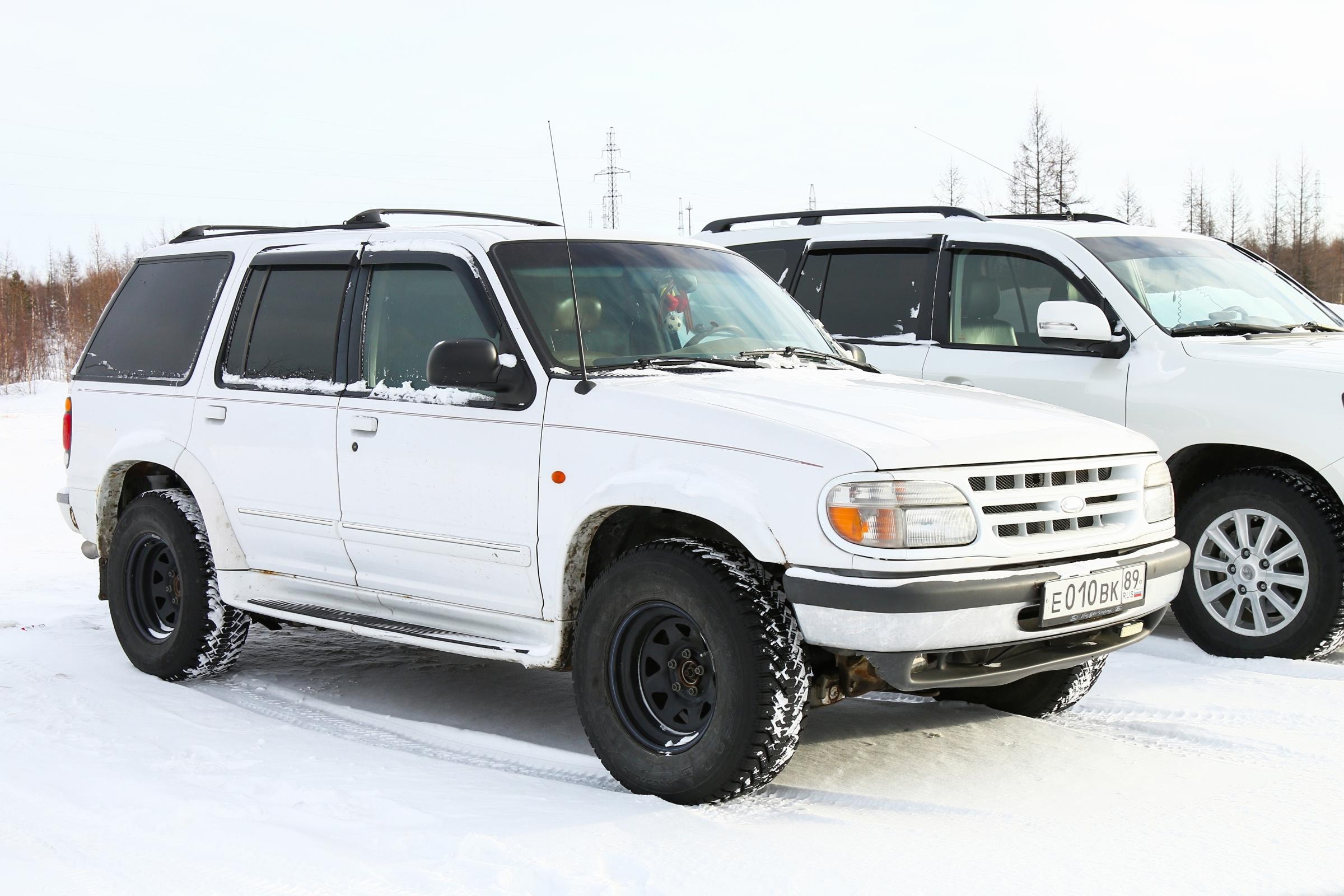Zwei weiße Ford Explorer Oldtimer sind seitlich auf einer verschneiten Straße geparkt.