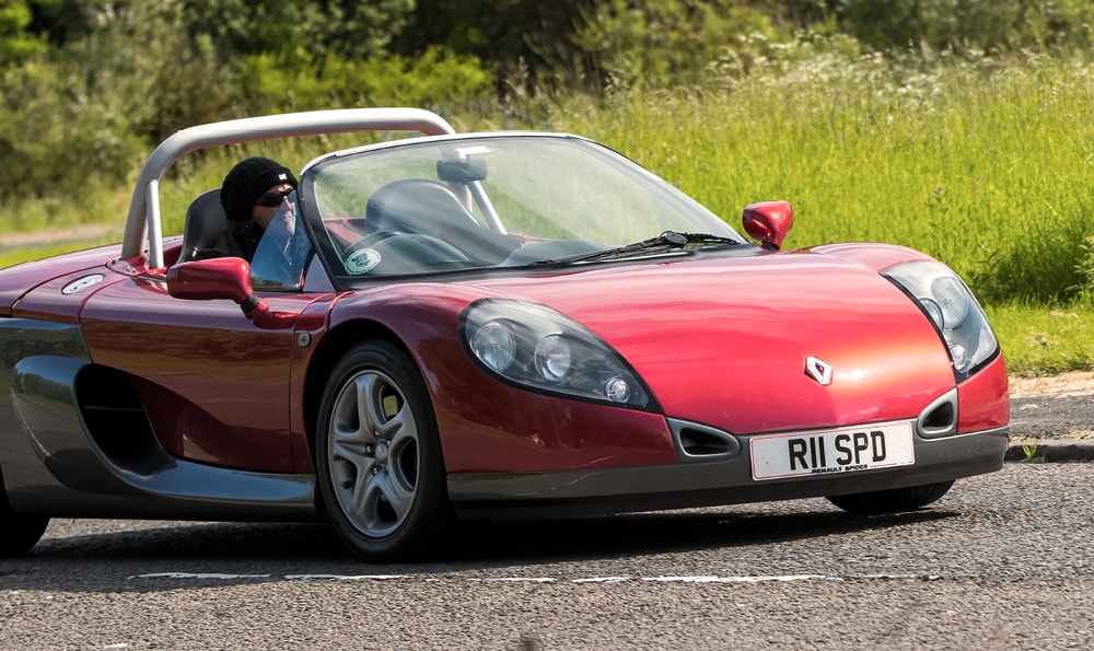 Zu den neue Oldtimer 2025 gehört der Renault Sport Spider. Hier in rot auf einer Straße mit Fahrer am Steuer.