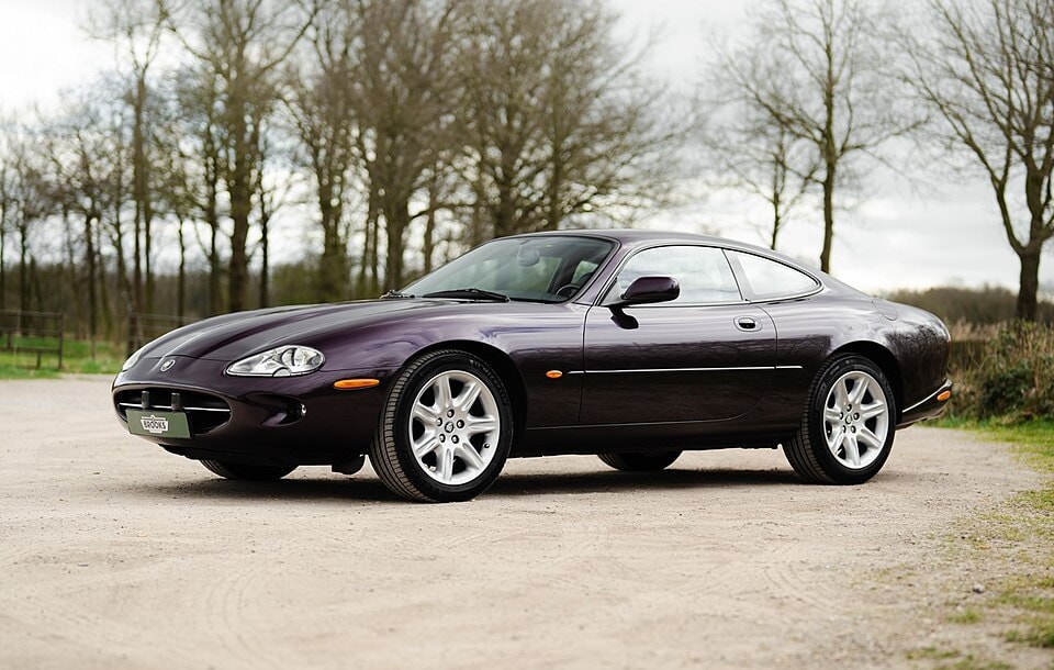 Lilafarbener Jaguar XK8 auf hellem Boden vor Bäumen, Seitenansicht