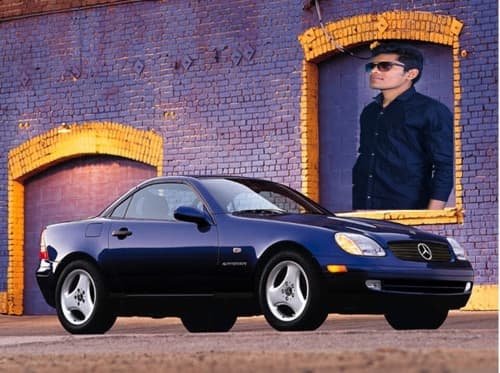 Blauer Mercedes SLK mit geschlossenem Metall-Verdeck vor lila Fabrikfassade, Ansicht schräg vorne