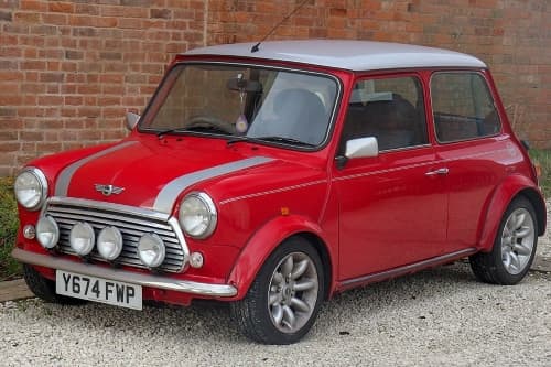 Mini 1.3 Cooper in Rot steht vor einer Backstein-Wand, Ansicht von schräg vorne