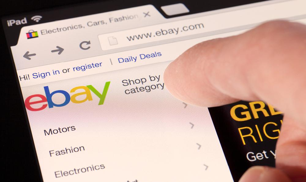 Finger zeigt auf die geöffnete Startseite von eBay im Browser auf den Button "Shop by category"