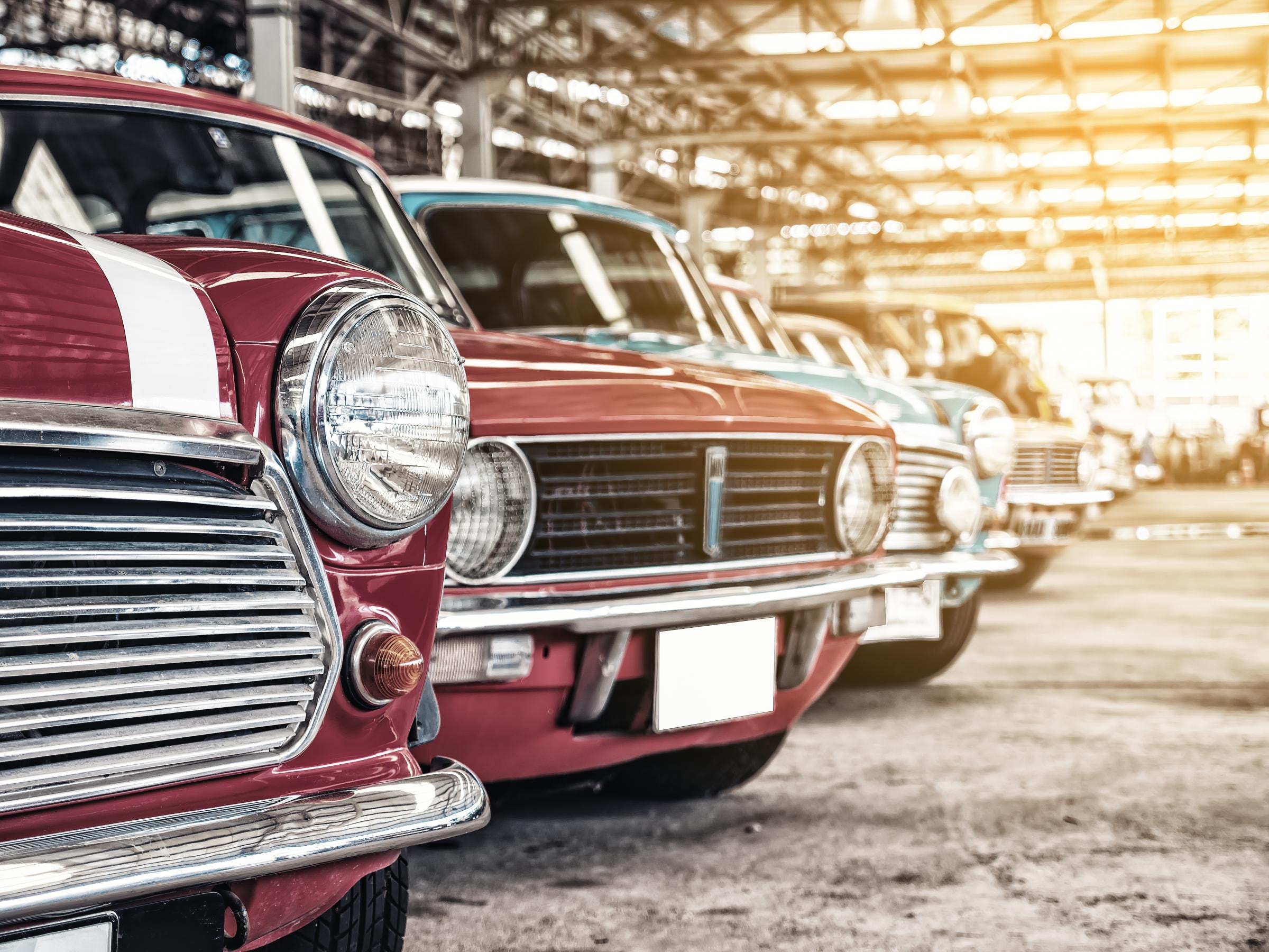 Mehrere Oldtimer stehen nebeneinander in einer sonnendurchfluteten Garage