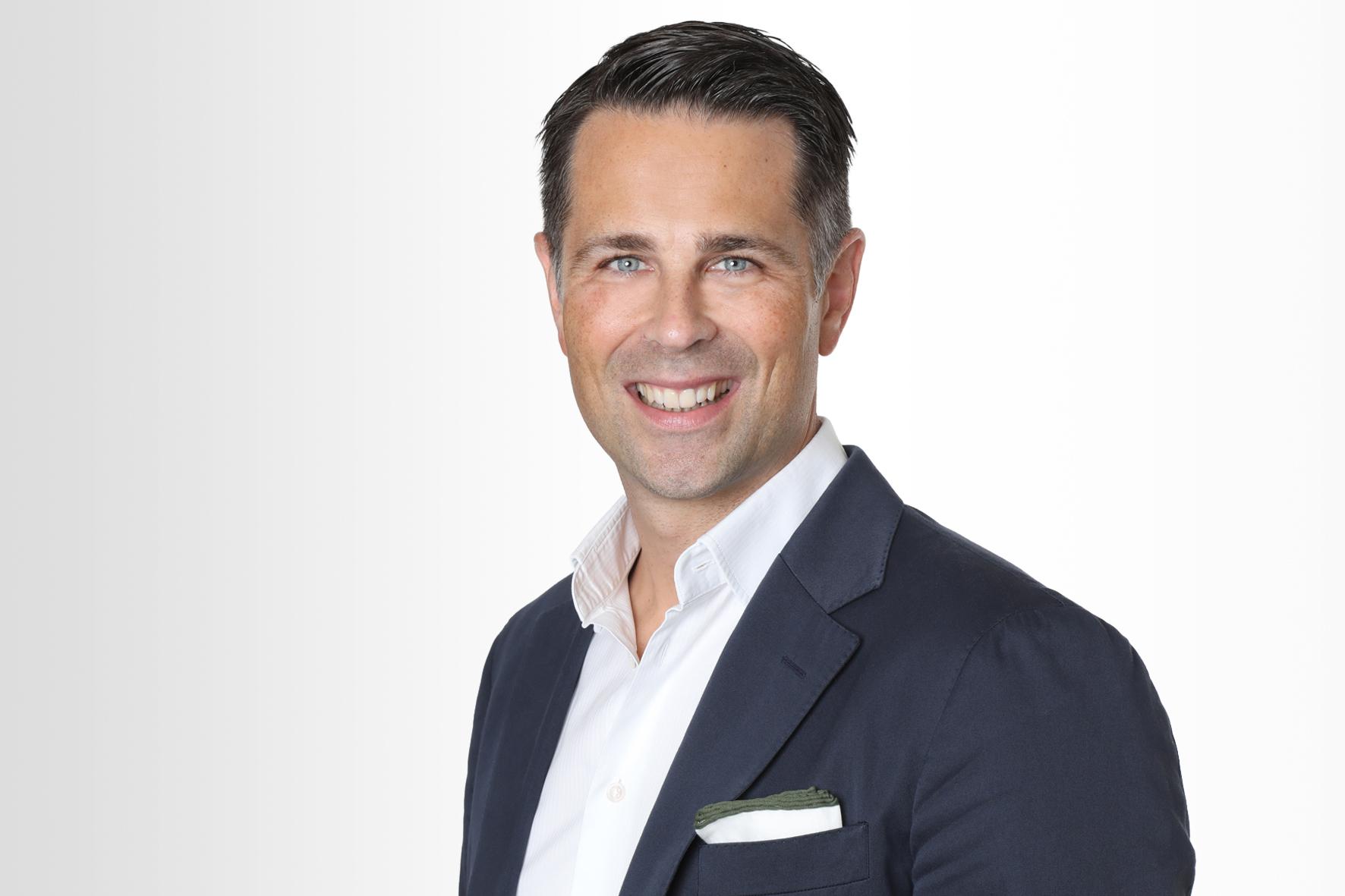 Der Deutschland-Chef von Hiscox Tim Bethge trägt ein dunkles Sakko und weißes Hemd und lächelt in die Kamera