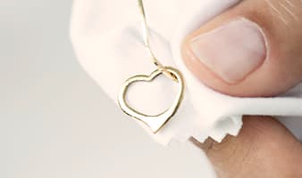 Eine Goldkette mit einem Herzförmigen Anhänger liegt wird von einer Hand auf einem Poliertuch gehalten