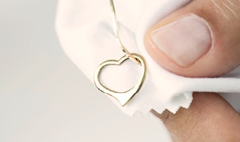 Eine Goldkette mit einem Herzförmigen Anhänger liegt wird von einer Hand auf einem Poliertuch gehalten