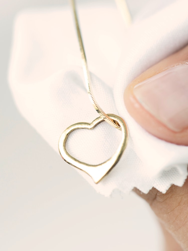 Eine Goldkette mit einem Herzförmigen Anhänger liegt wird von einer Hand auf einem Poliertuch gehalten