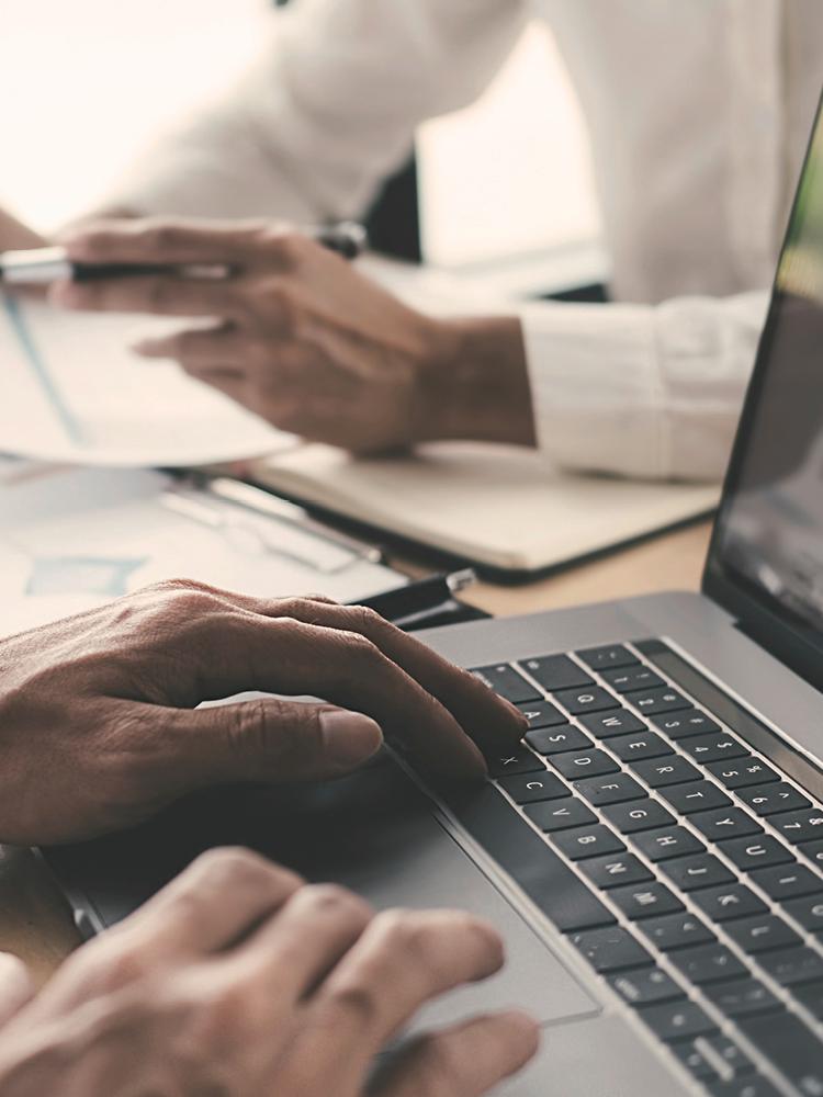 Zwei unbekannte Männer arbeiten an einem Laptop und an Dokumenten