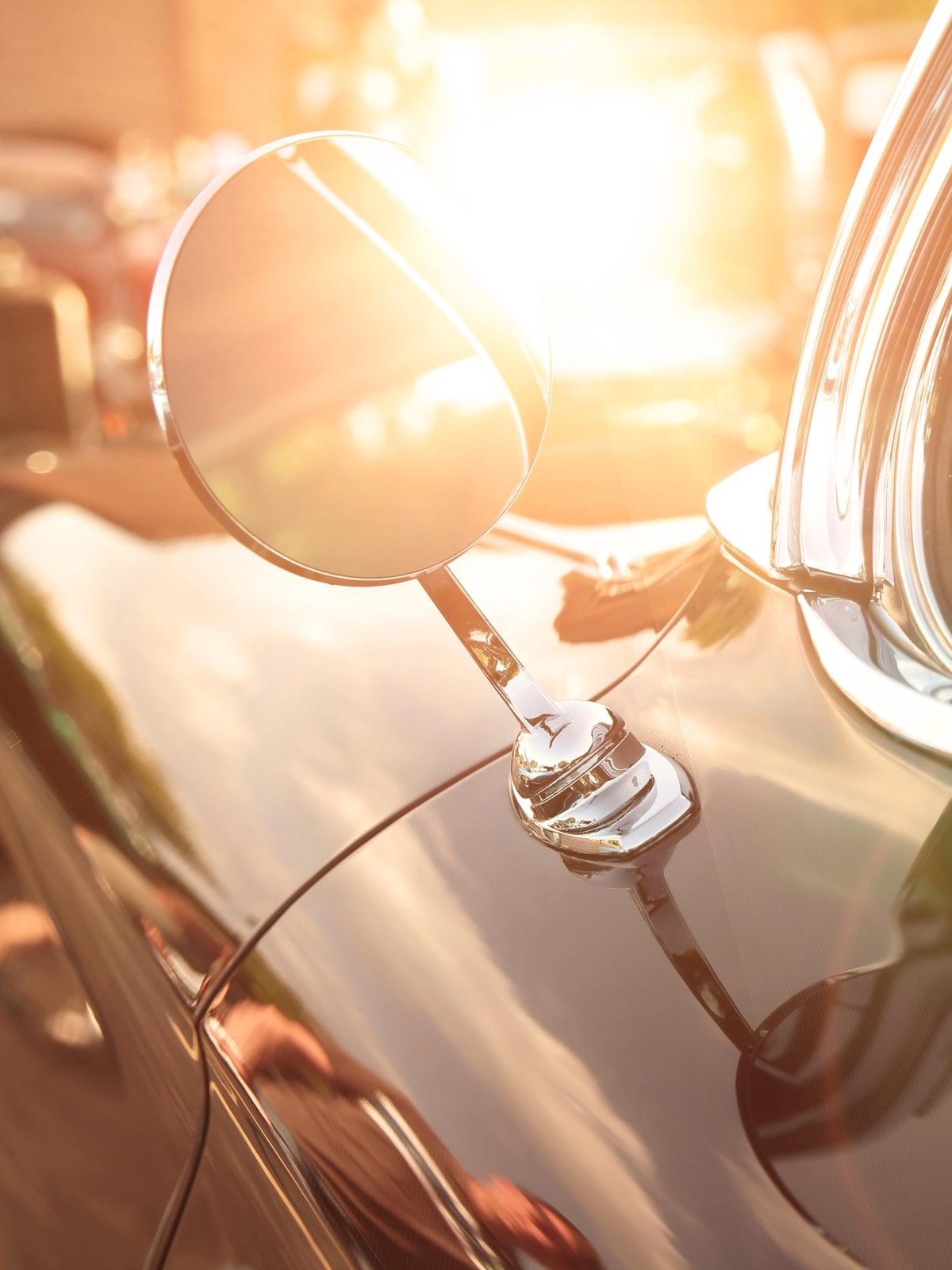 Nahaufnahme eines Seitenspiegels und Fensters eines klassischen Autos, das Sonnenlicht mit einem warmen Glanz reflektiert. Das Bild fängt die glatte, glänzende Oberfläche des Autos und das nostalgische Gefühl von Oldtimern ein.