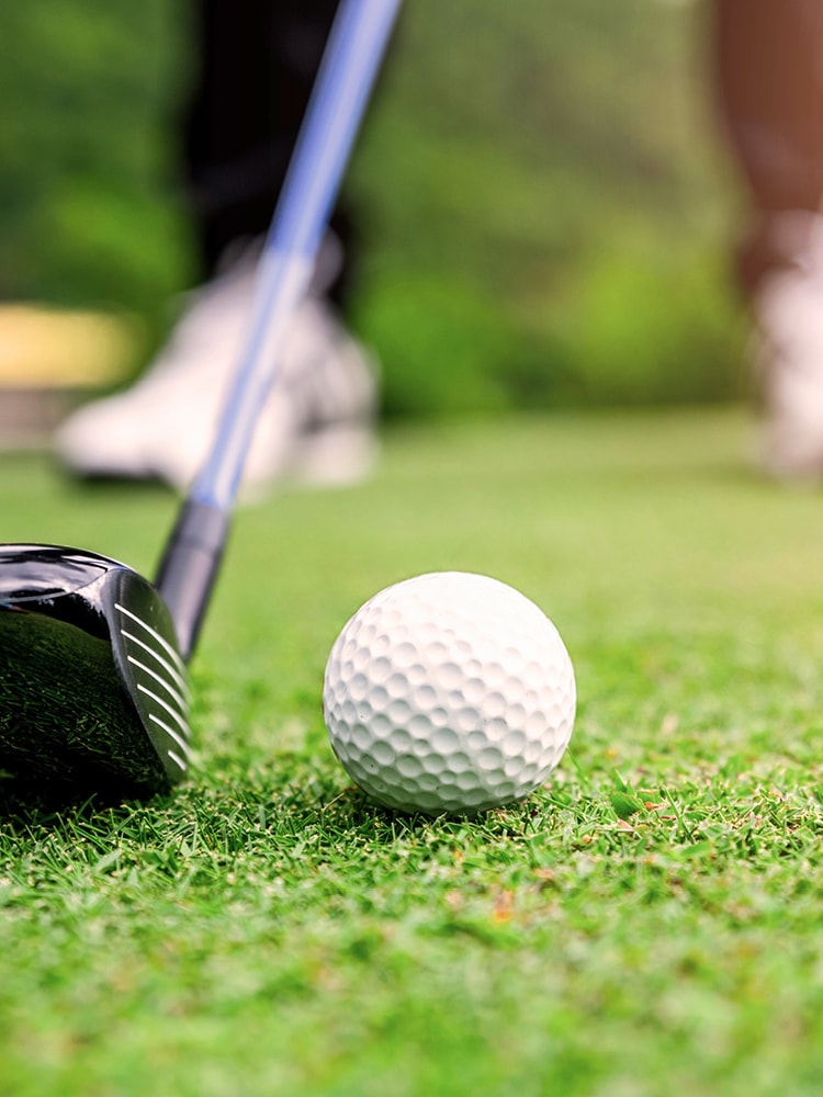 Golfball auf dem Grün vor einem Schläger, unscharfer Hintergrund mit Golfer.