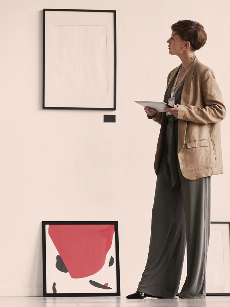 Eine Frau mit Blazer steht vor einer Wand mit Kunstwerken