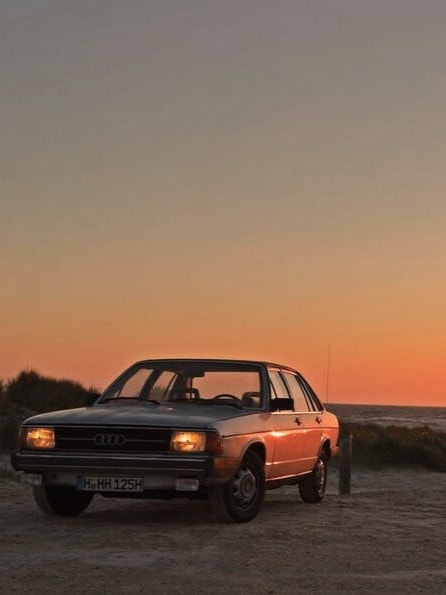 Ein Audi 100 Typ 43, ein Oldtimer, parkt bei Sonnenuntergang am Strand.