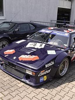 Auf einer Ziegelstein-Auffahrt sind zwei Oldtimer geparkt, davon ist einer der BMW M1.